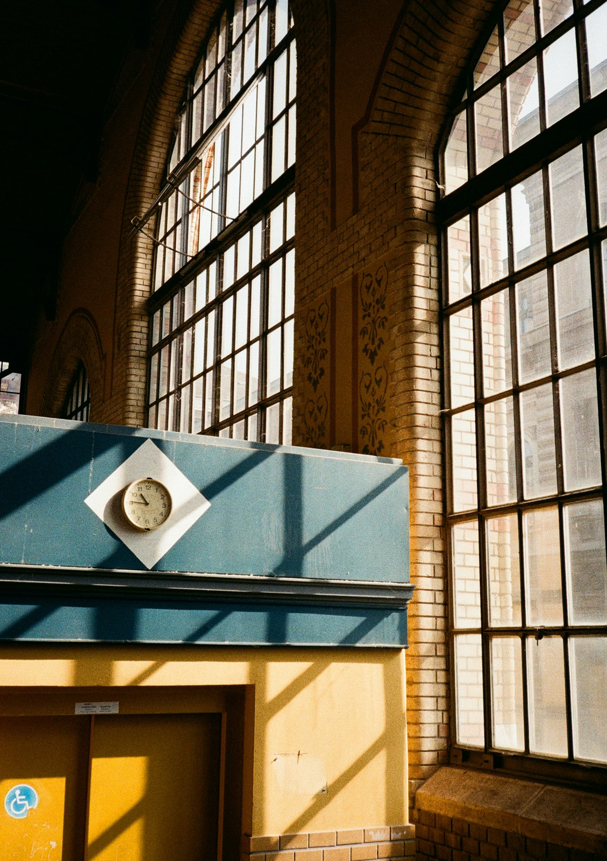 Tall arched windows and a wall clock cast long shadows across the floor of an empty interior.