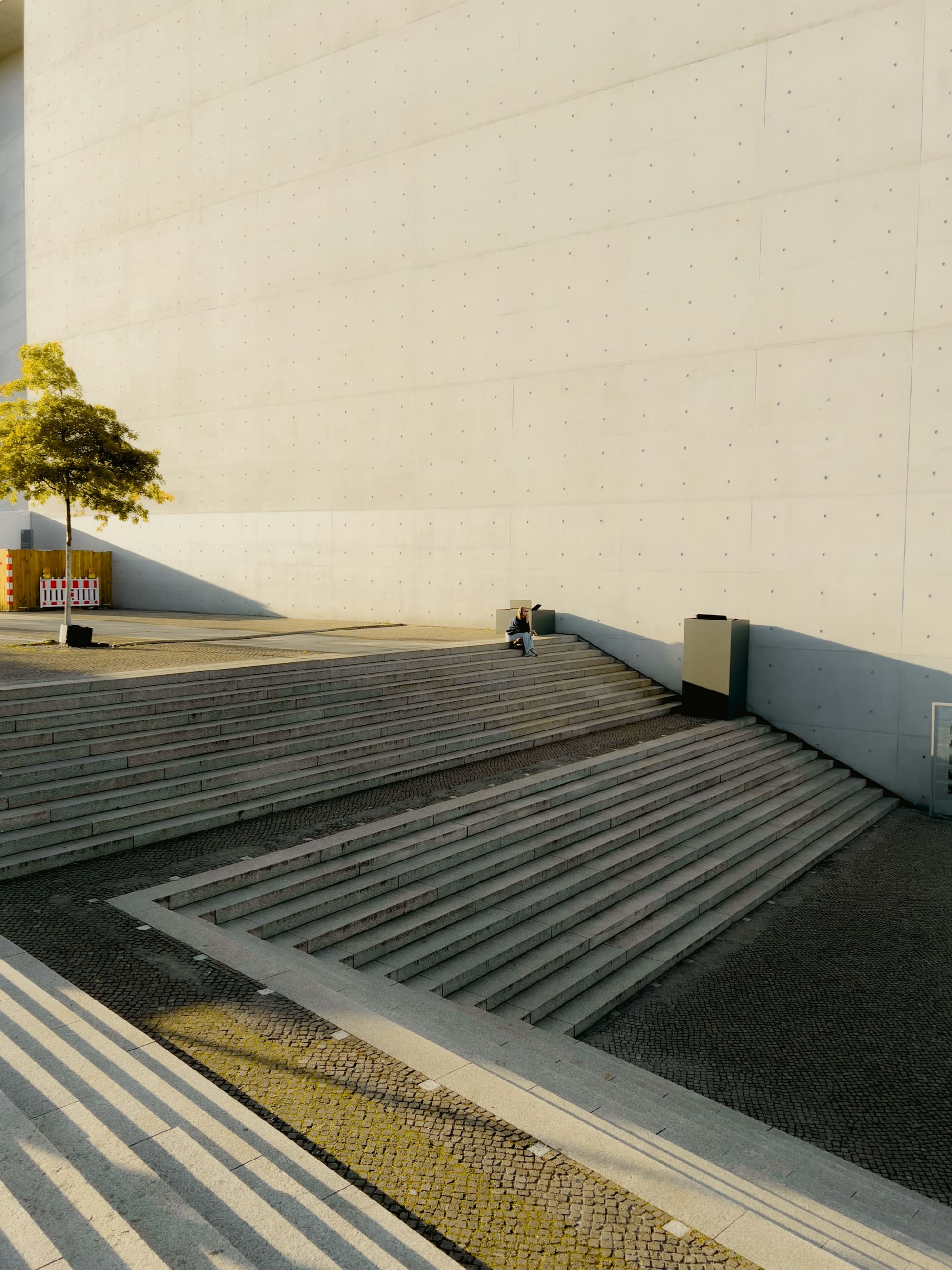 Concrete stairs rise toward a building entrance, with strong light and shadow shaping the steps and walls.