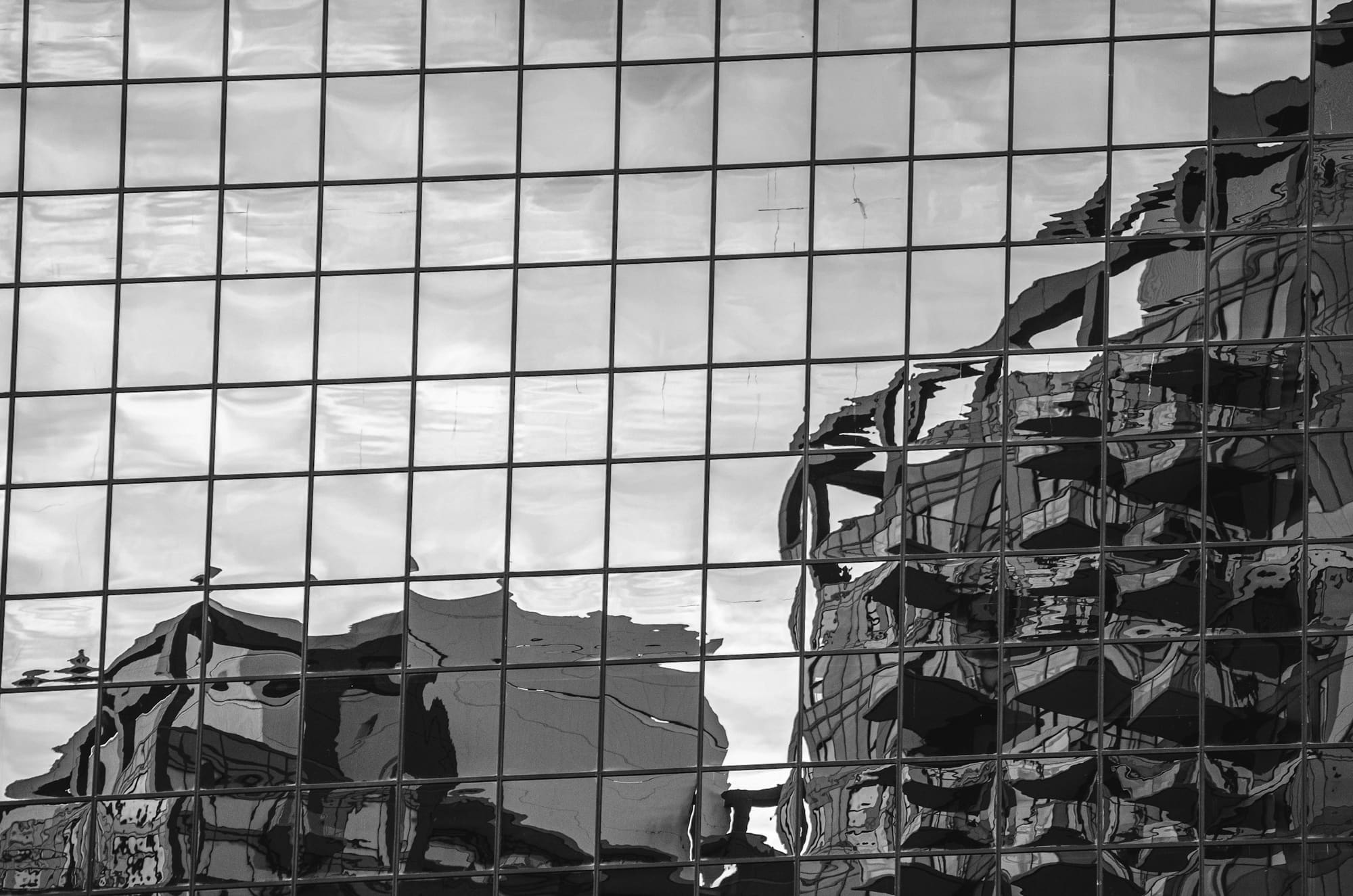 A grid of windowpanes reflects distorted city buildings in a layered black-and-white composition.